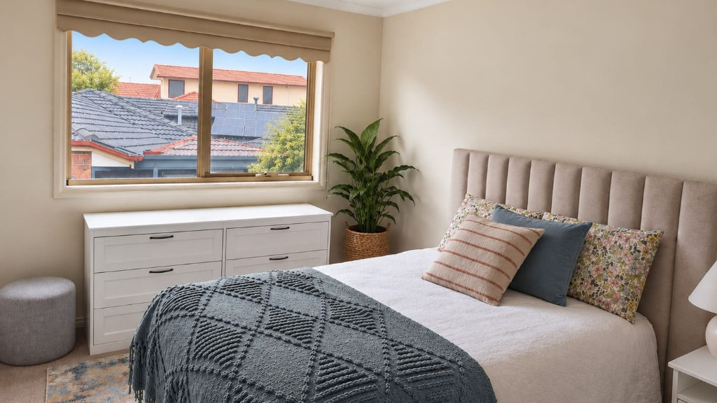A calm spare bedroom with a slate throw across the bed and a window looking over neighbouring roofs